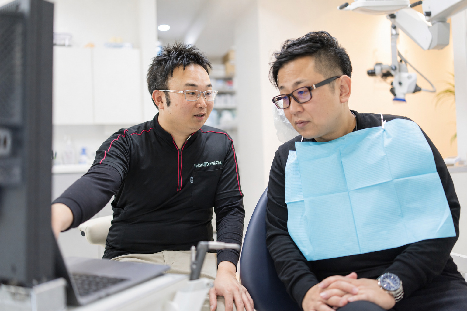モニター画面を見ながら男性患者に治療内容を説明する男性歯科医師のカウンセリング風景