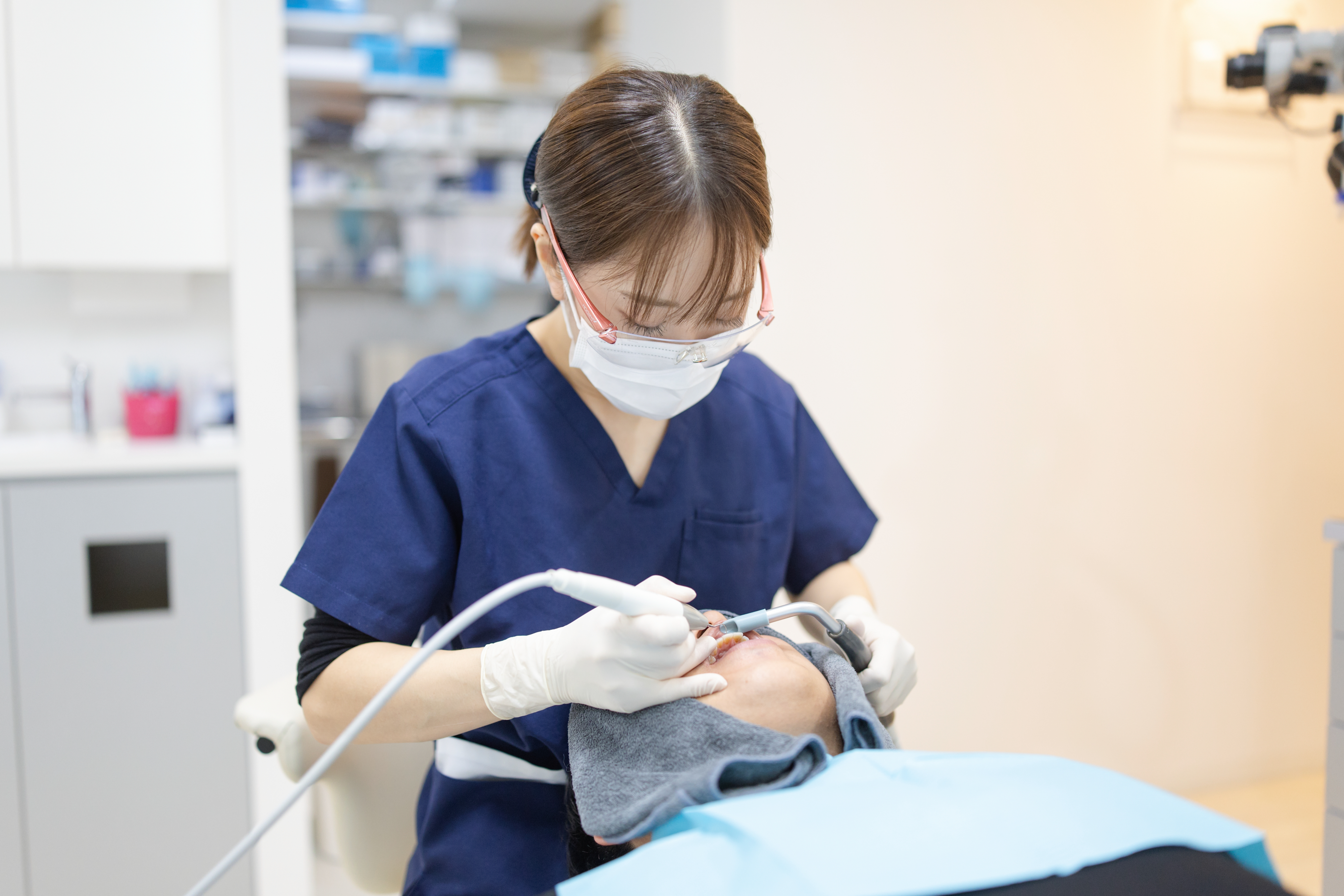 紺色のスクラブを着用し患者の歯のクリーニング・治療を行う女性歯科衛生士