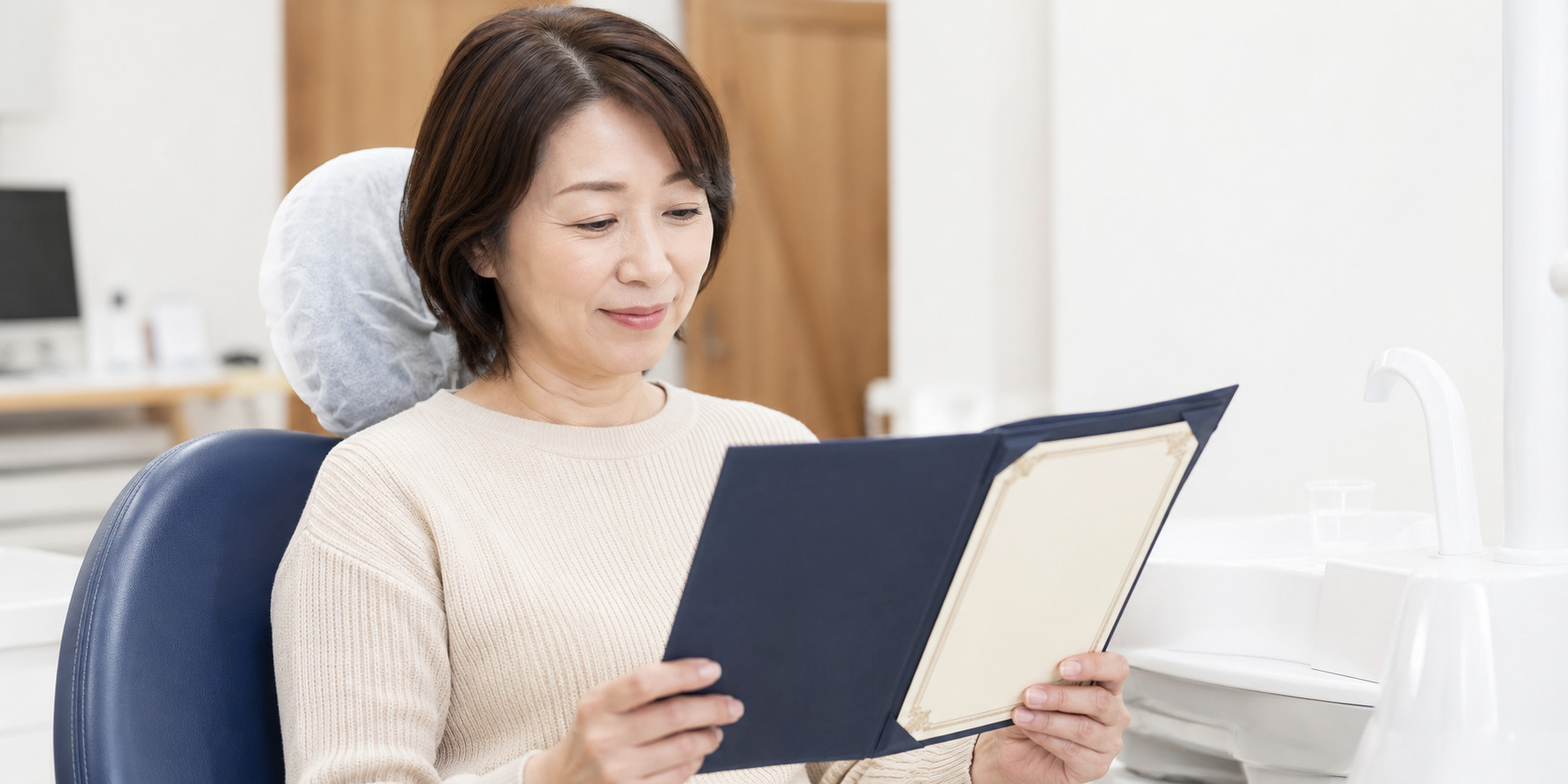 診療チェアで治療説明のパンフレットを読む笑顔の中高年女性患者