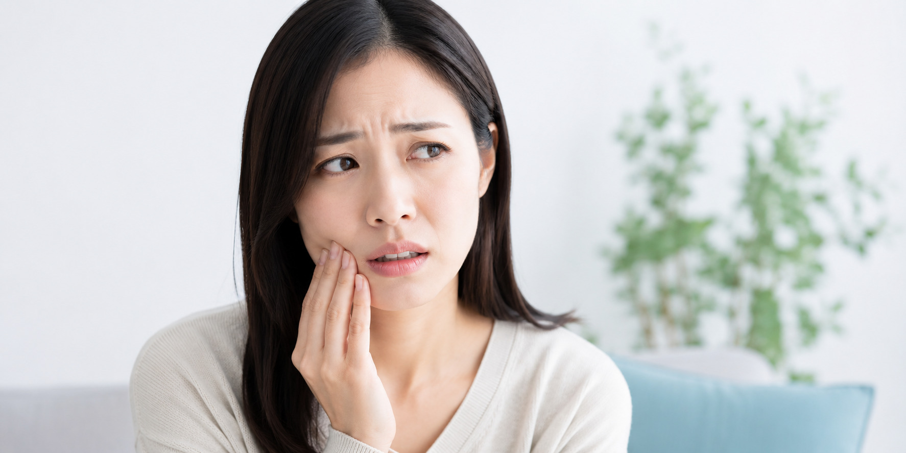 歯の痛みで頬に手を当て、つらそうな表情を浮かべる若い日本人女性